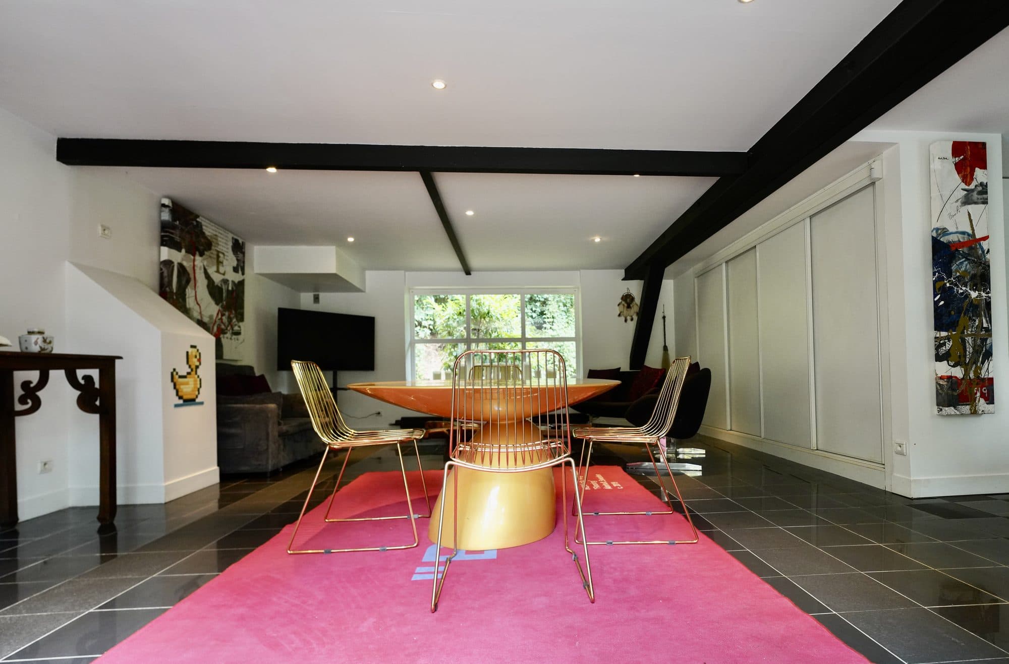 Le séjour de l'appartement design, tapis rose et table dorée sous les poutres noires