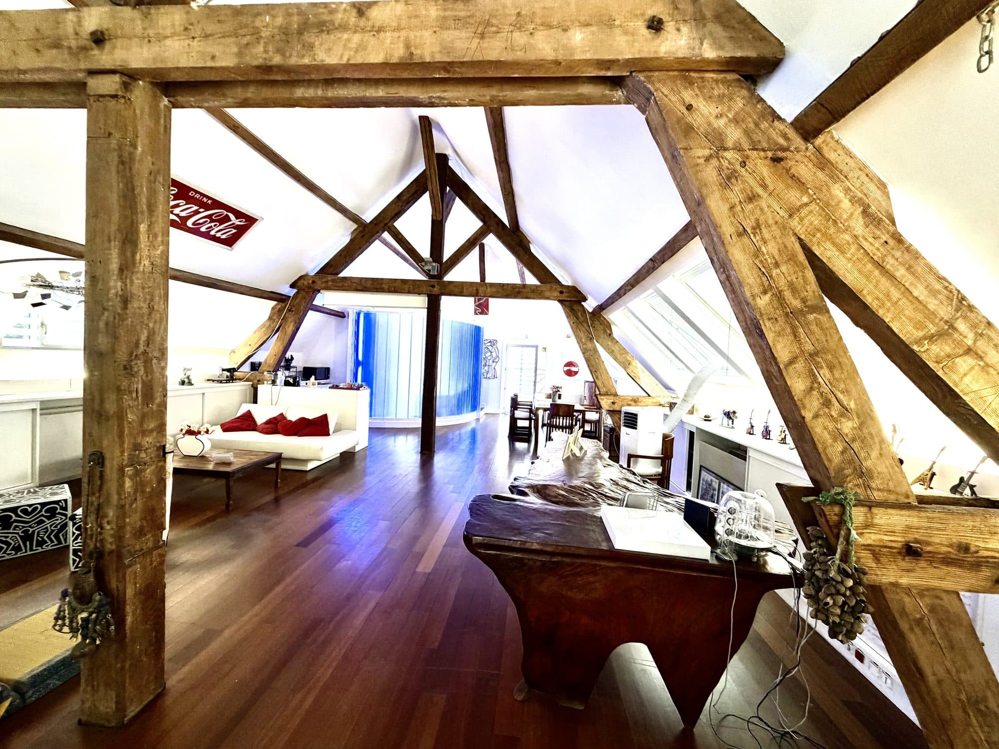 Le grand salon du loft sous la charpente apparente, canapé blanc et parquet